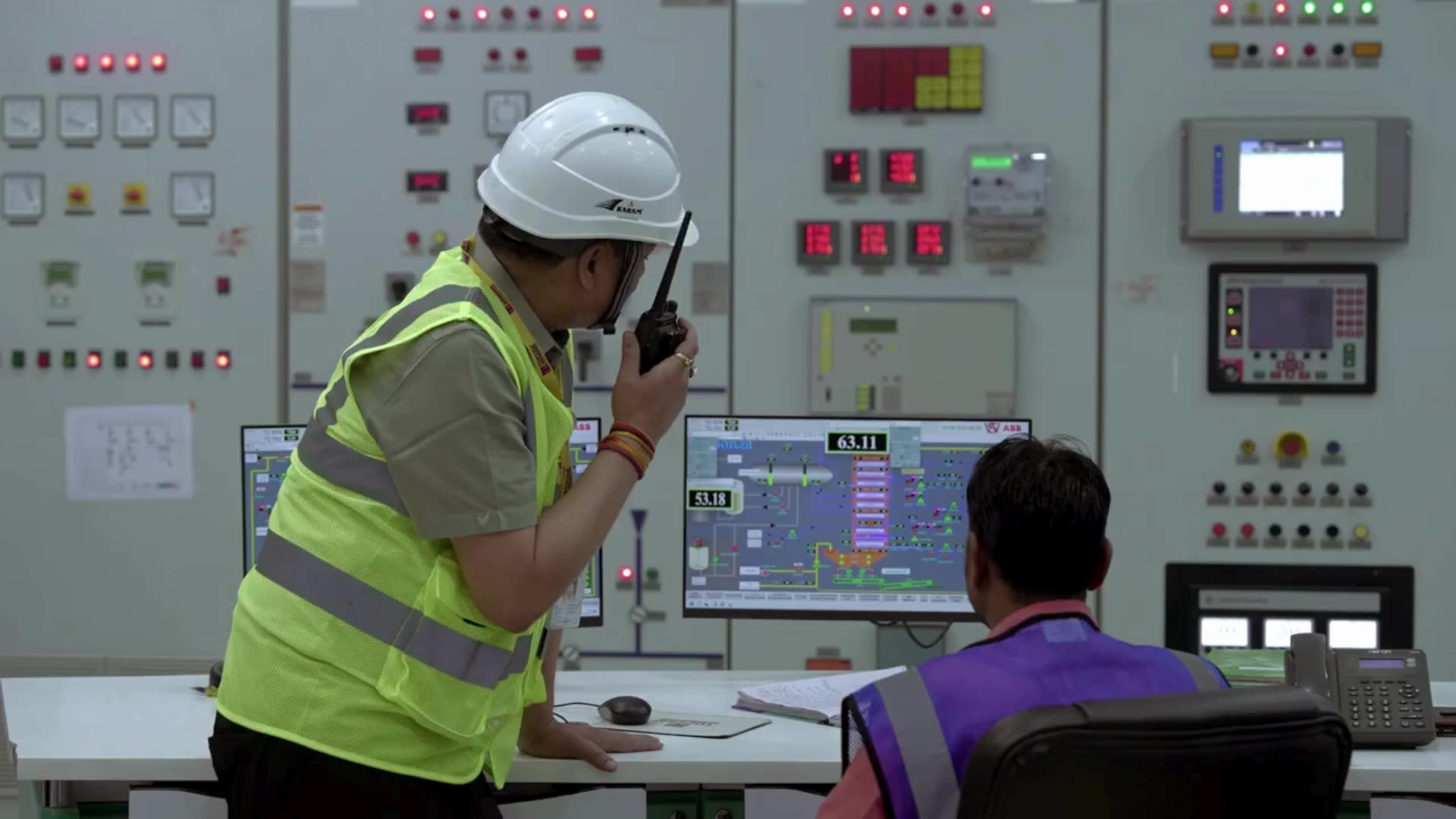 A plant engineer in a hard hat and hi-vis vest at a control room console